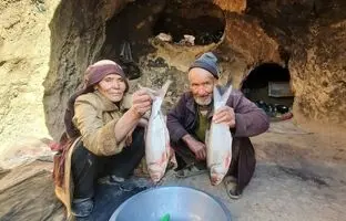 (ویدئو) سرخ کردن دو ماهی آزاد روی ساج توسط زوج مسن غارنشین افغانستانی